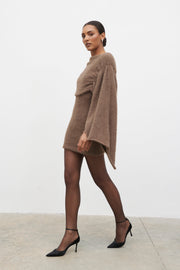 Woman wearing a brown sweater dress with black stockings and shoes on a white background