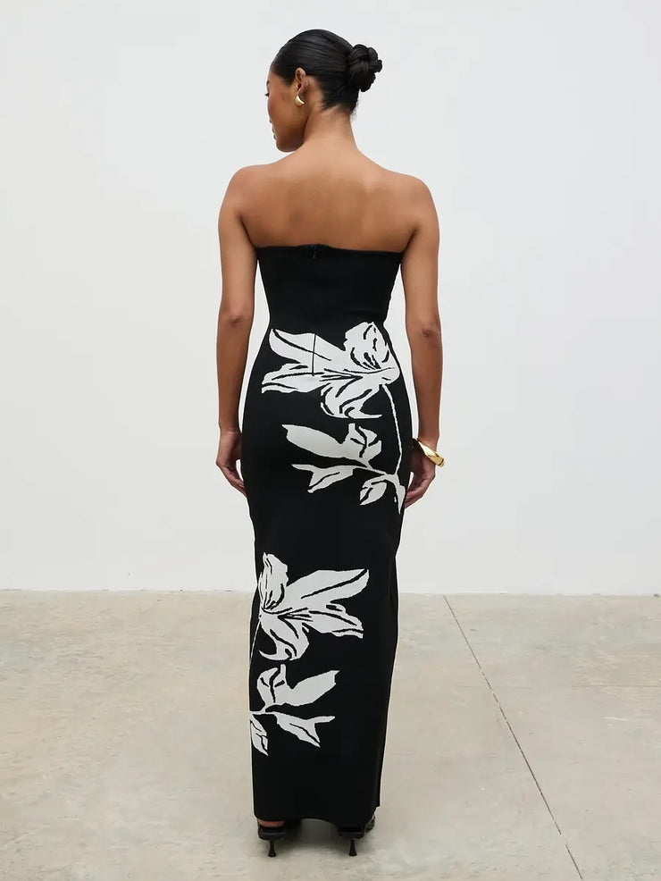 Woman wearing a black strapless dress with white floral patterns on a plain background