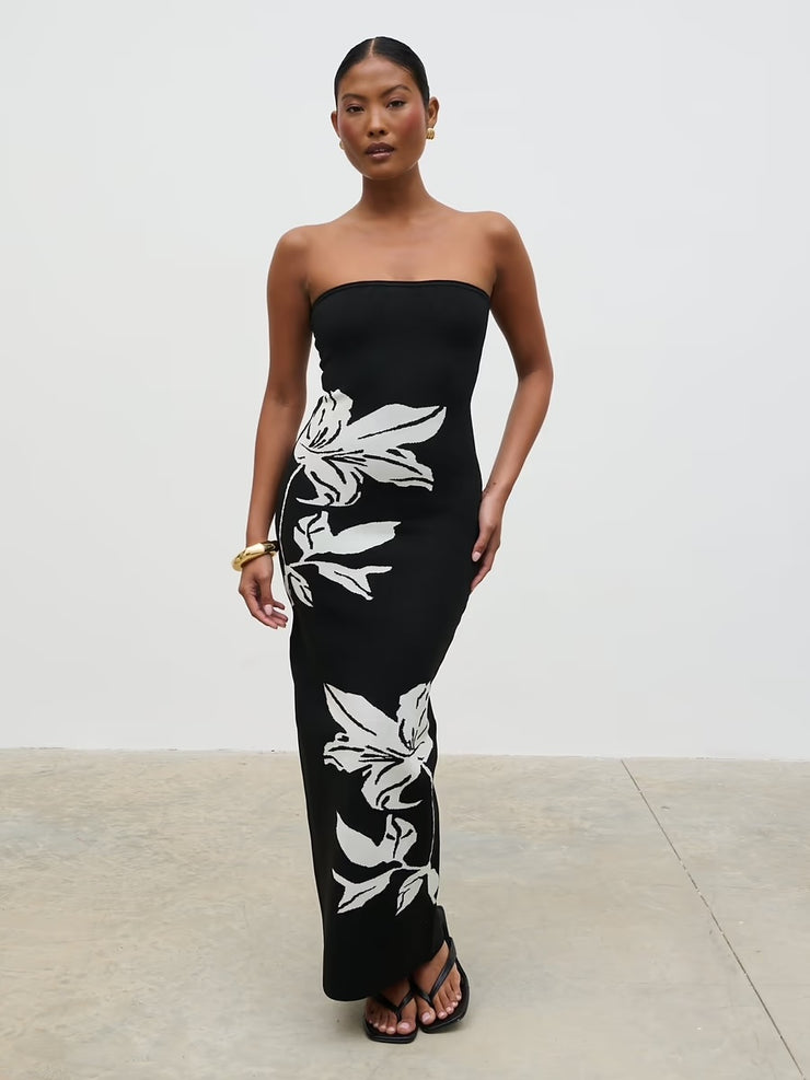 Woman wearing a black strapless dress with white floral patterns on a plain background