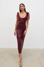 Woman wearing a burgundy sequin dress with bow sleeves against a white background