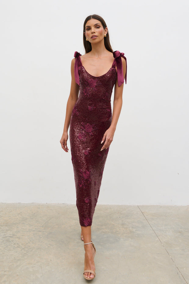 Woman wearing a burgundy sequin dress with bow sleeves against a white background