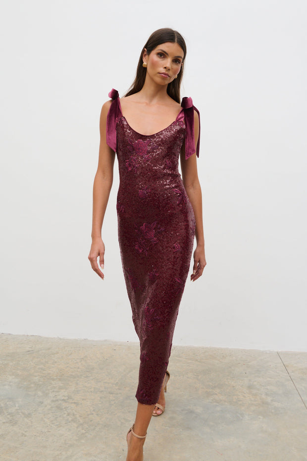 Woman wearing a burgundy sequin dress with purple accents against a white background