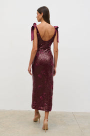 Woman wearing a burgundy sequin dress with bow straps on a white background