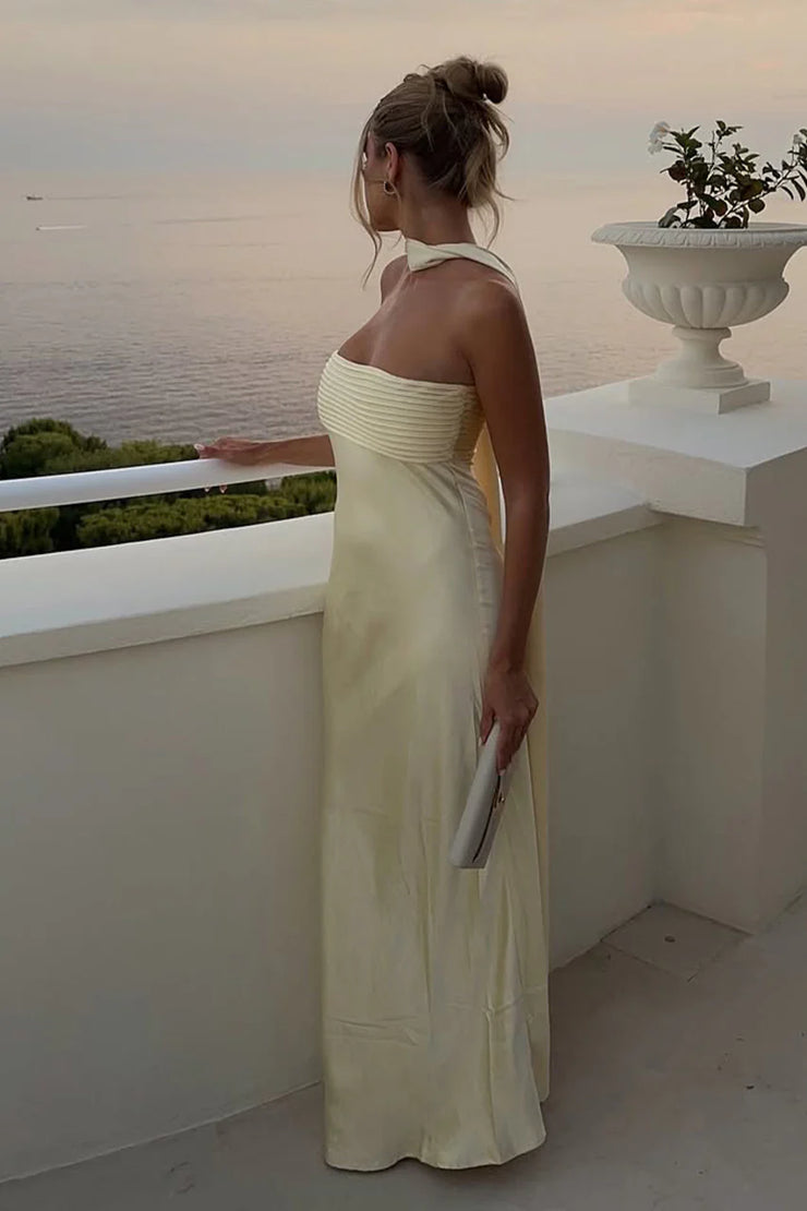 Woman in a strapless dress standing on a balcony overlooking the ocean at sunset.