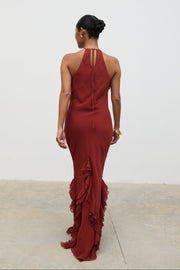Woman wearing a burgundy evening gown with ruffled details on a plain background