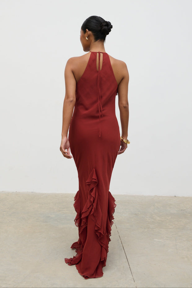 Woman wearing a burgundy evening gown with ruffled details on a plain background