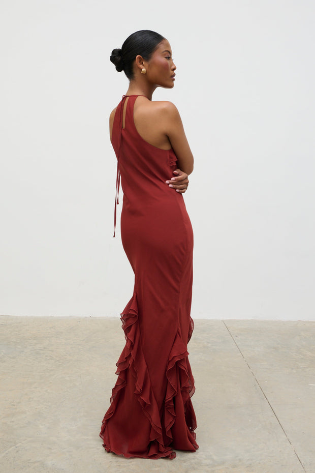 Woman wearing a burgundy one-shoulder dress with ruffles in a minimalistic setting