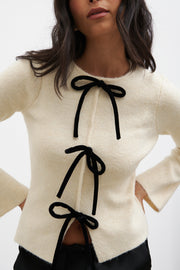 Woman wearing a cream sweater with black ribbons on a white background