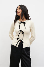 Woman wearing a white sweater with black ribbons against a white background