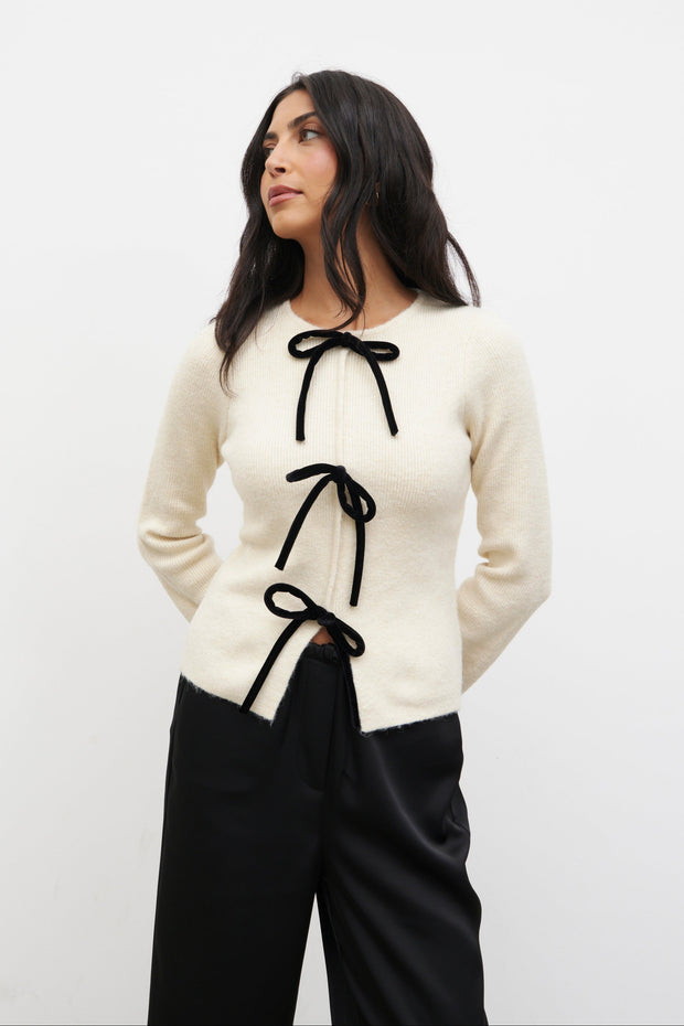 Woman wearing a white sweater with black ribbons against a white background