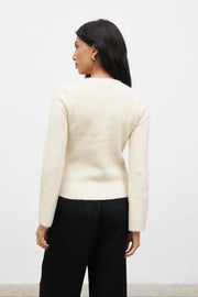 Woman wearing a cream sweater and black pants against a white background