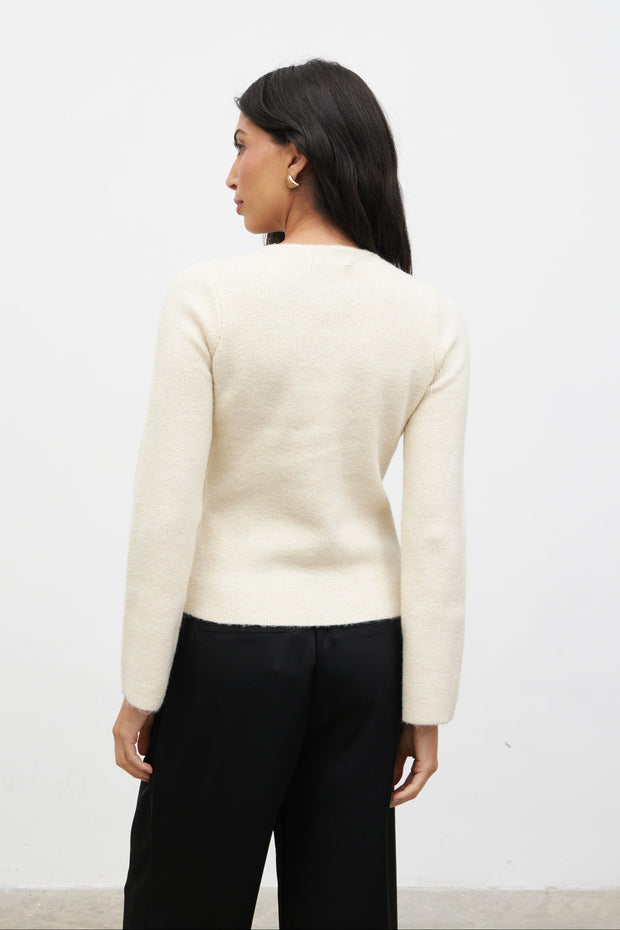 Woman wearing a cream sweater and black pants against a white background